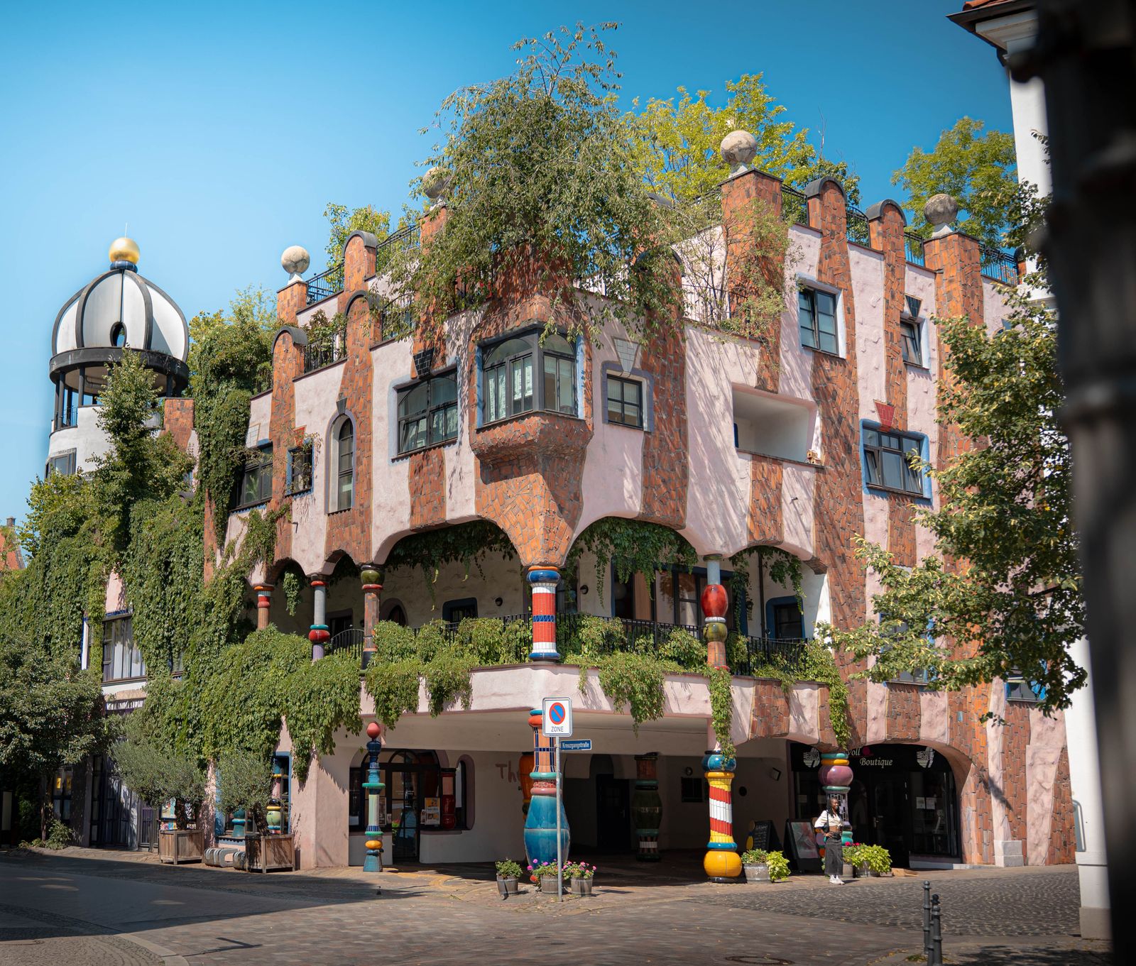 Farbenfrohes Hundertwasser-Haus mit bunten Säulen und begrünten Balkonen