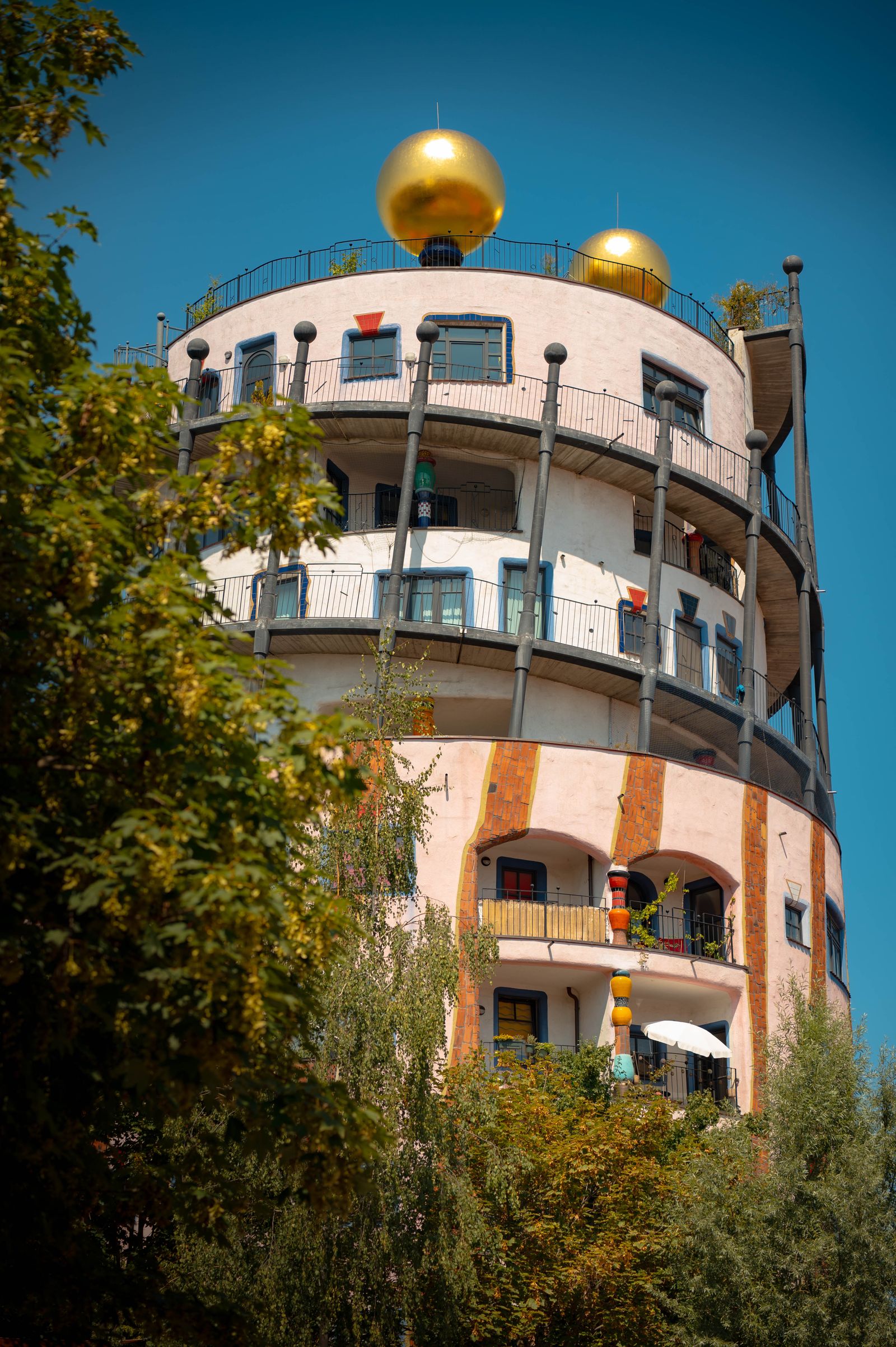 Runder Hundertwasser-Turm mit goldenen Kugeln vor tiefblauem Himmel