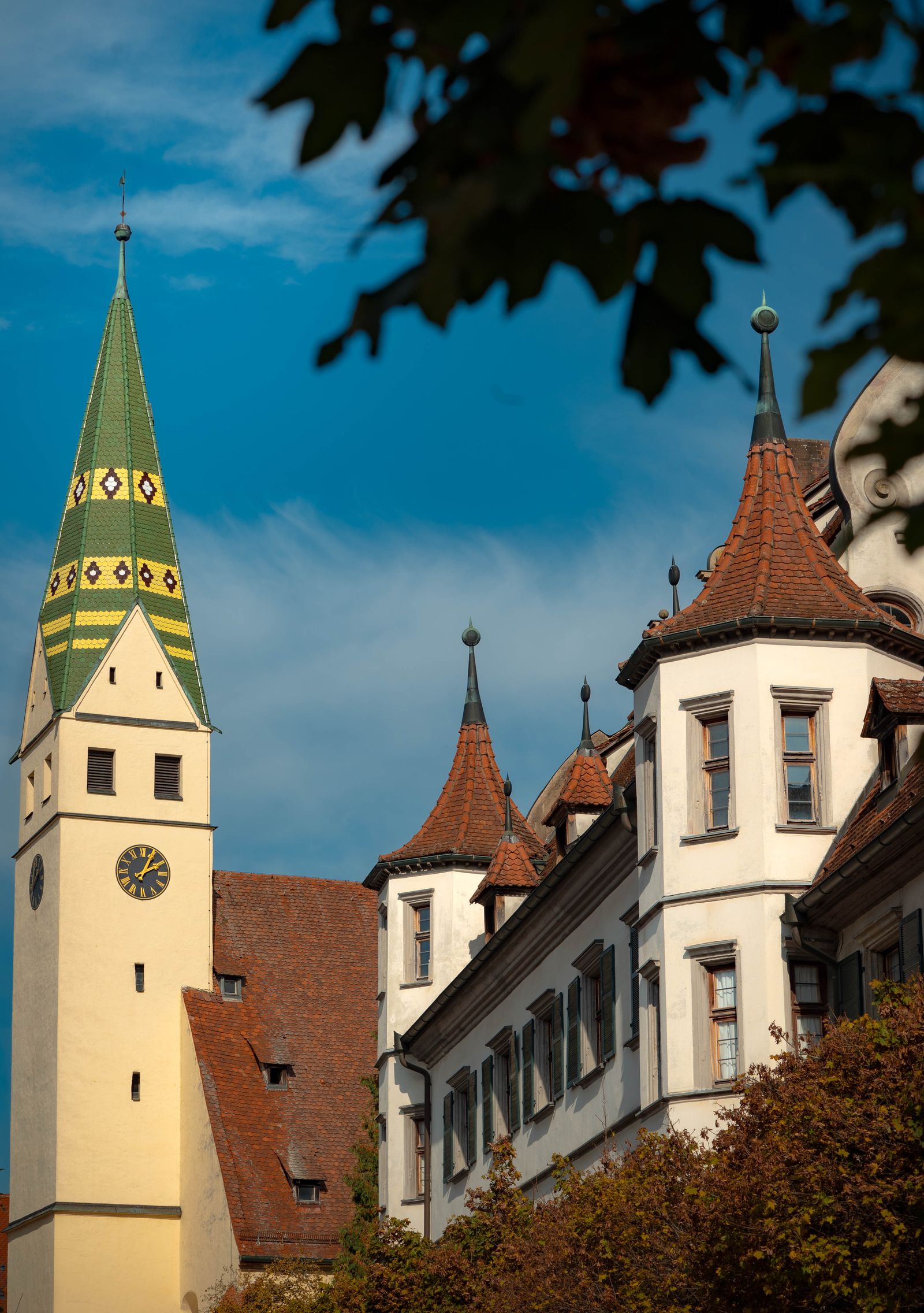 Kirchturm mit grün-gelb gemustertem Dach neben Schlosstürmen vor blauem Himmel