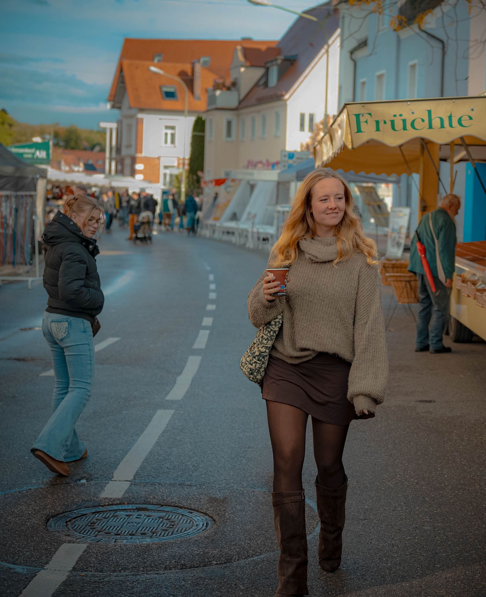 Frau mit Kaffeebecher schlendert über einen herbstlichen Markt