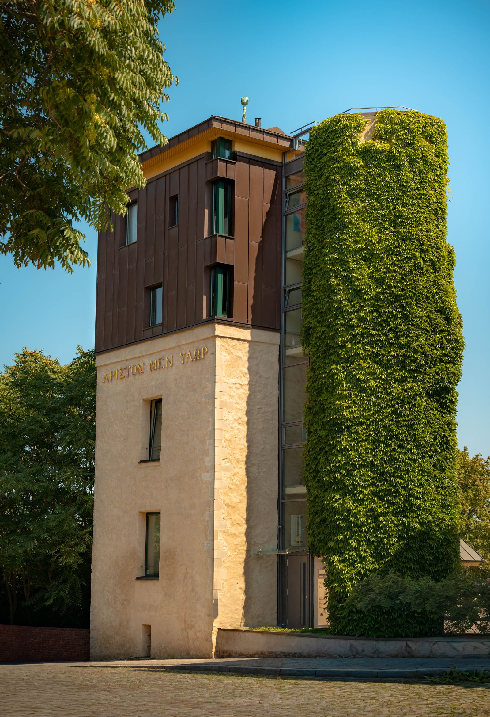 Alter Wasserturm mit Kupferfassade neben einem dicht mit Efeu bewachsenen Turm